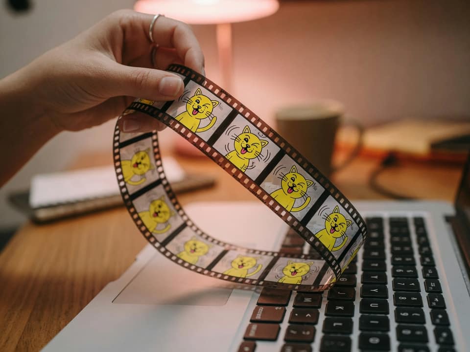 Dropping a printed film strip of cartoon frames onto a laptop to compress a GIF